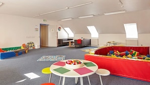 A spacious playroom with a high ceiling, skylights, and a variety of play structures and tables.