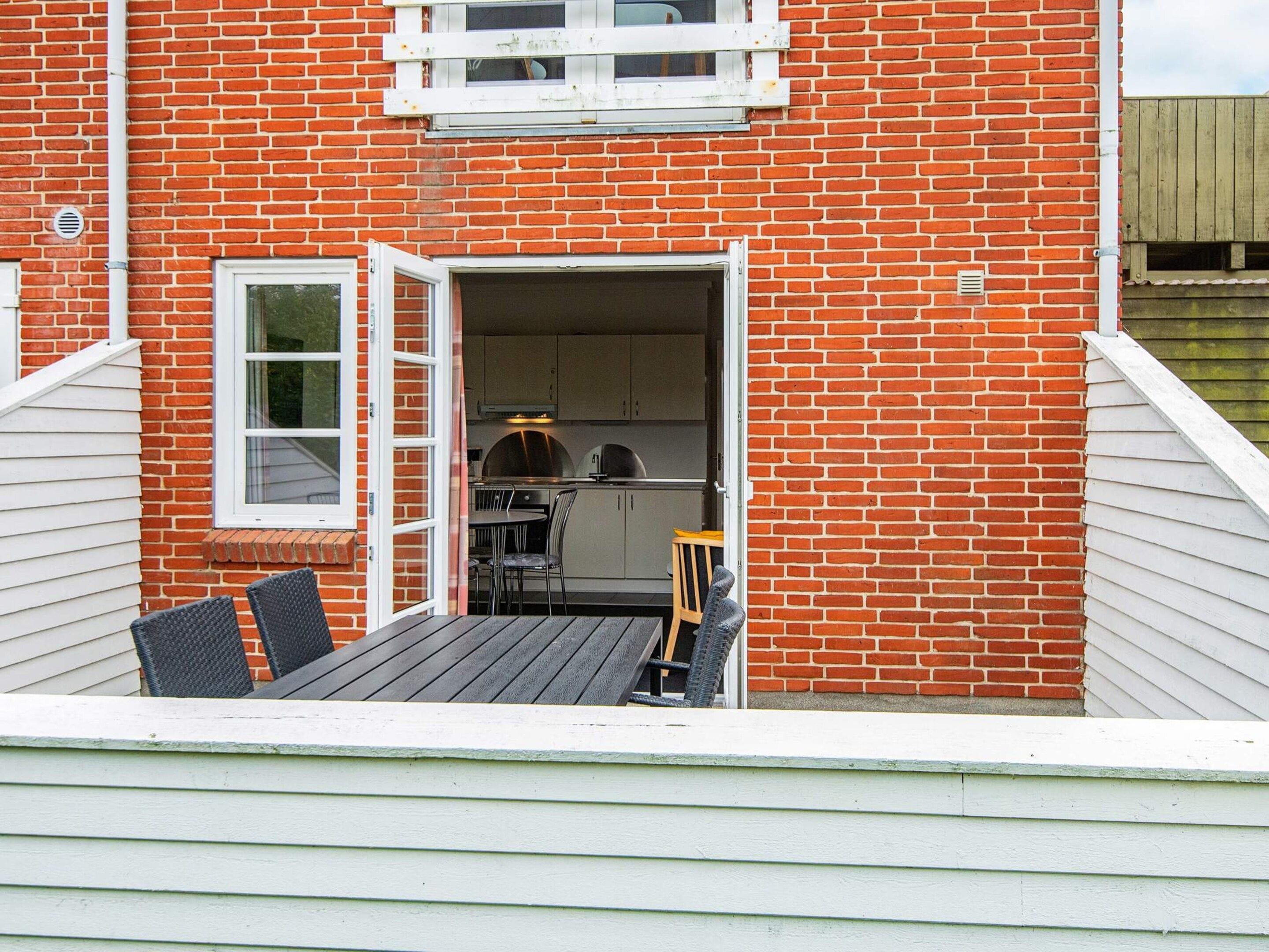 A brick building with a patio area featuring a table and chairs, a grill, and a window with a view of the interior.
