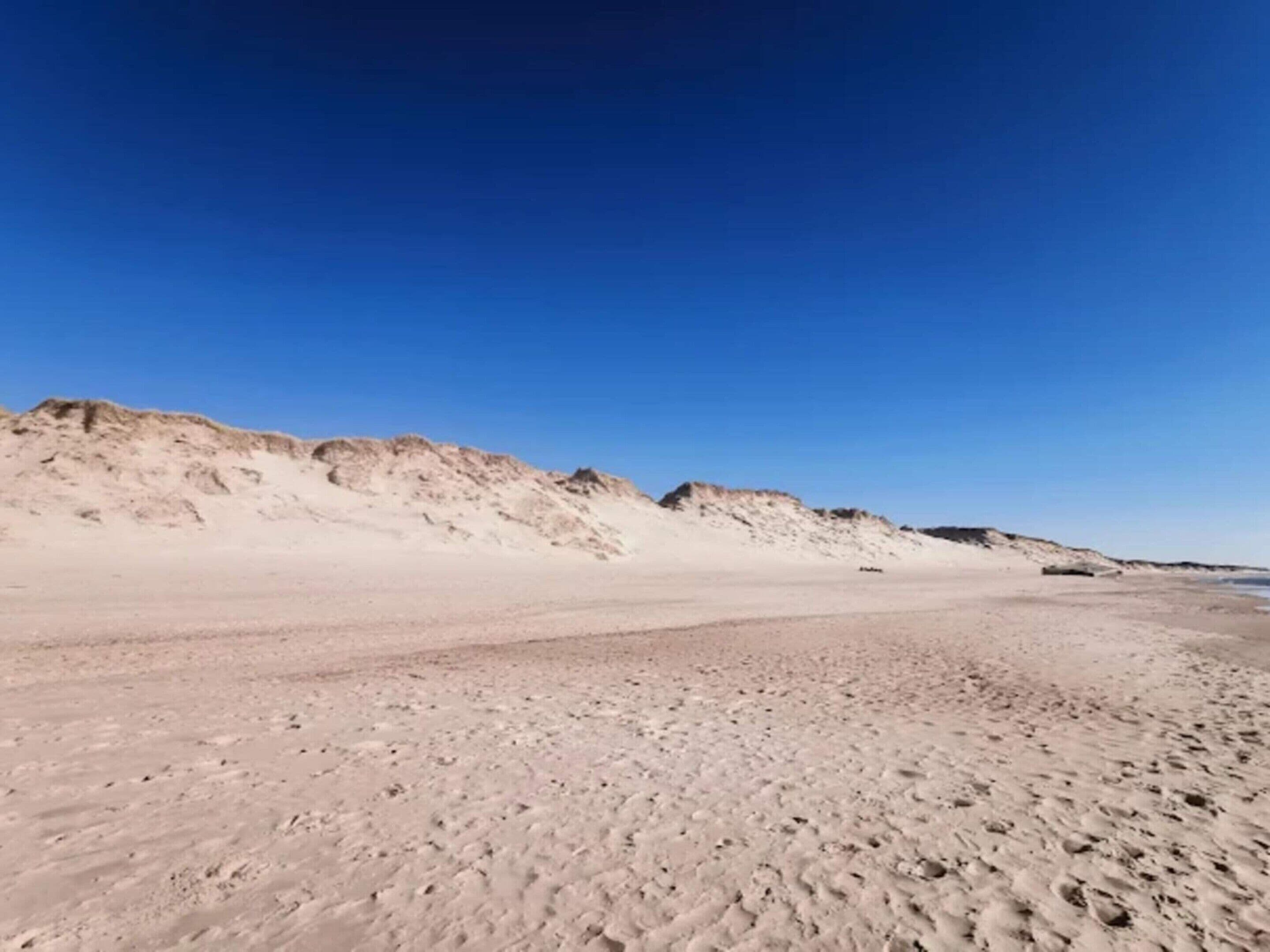 A sandy beach with dunes and a clear blue sky.