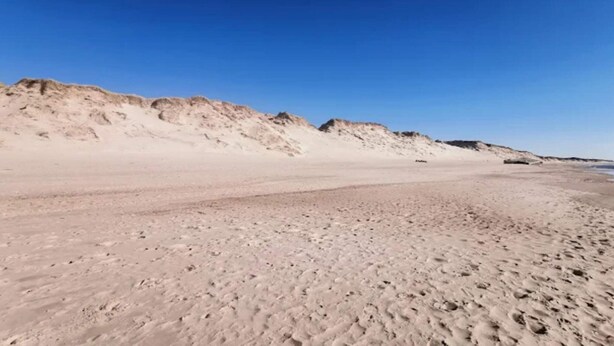 A sandy beach with dunes and a clear blue sky.