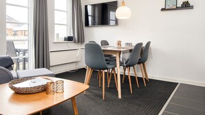 A modern dining area with a table, chairs, a TV mounted on the wall, and a small shelf with a picture.