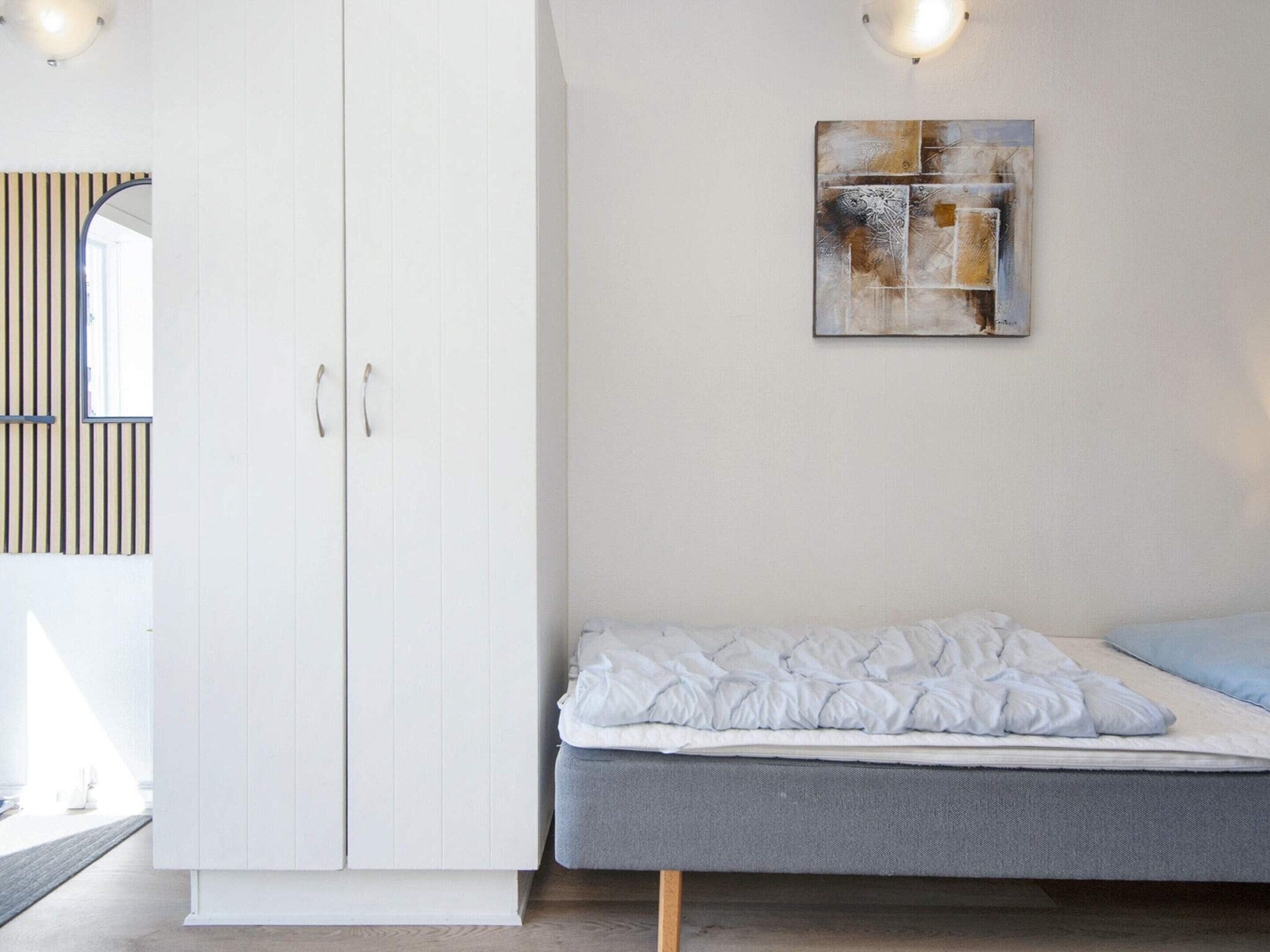 A bedroom with a bed, a wardrobe, and a wall-mounted abstract painting.