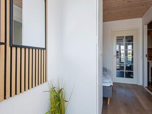 A hallway with a wooden slat wall, a potted plant, and a bed with a blue mattress in the background. - 5 Person Holiday Home in Romo (Rømø)