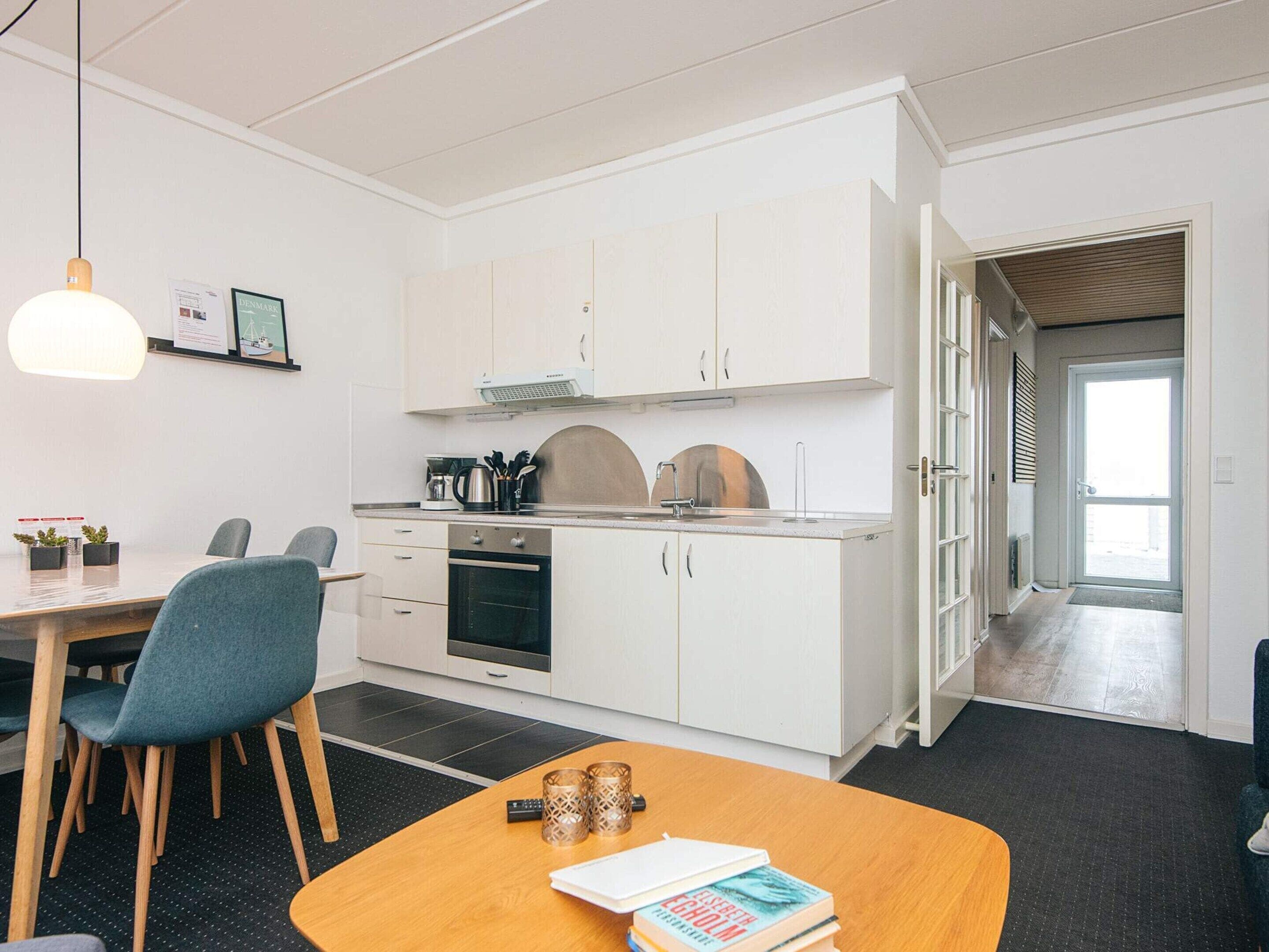 A modern kitchen with white cabinets, a dining area with a wooden table and chairs, and a view of the hallway.