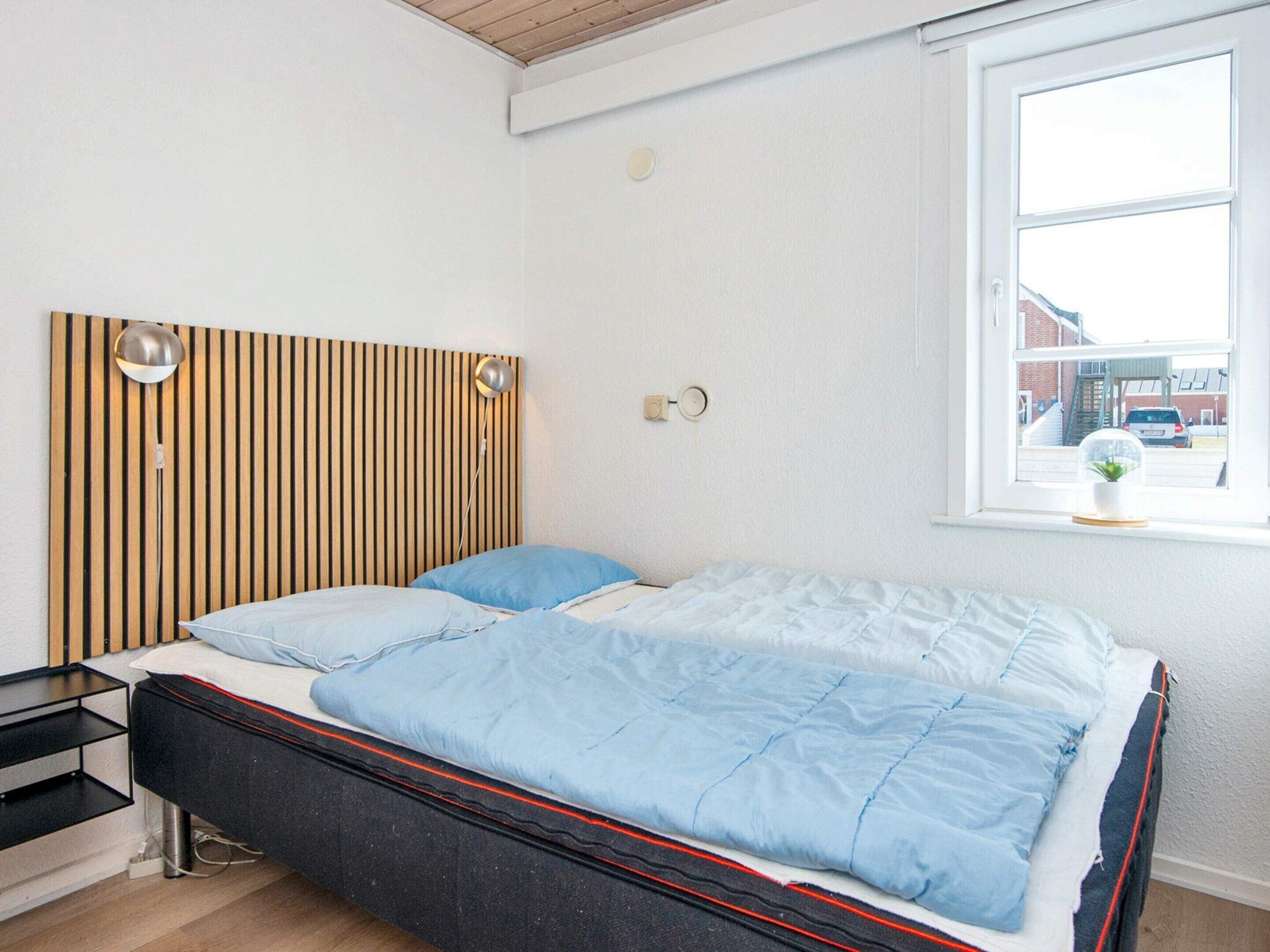 A bedroom with a bed, bedside table, lamp, and a window with a view of the outside.