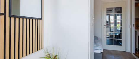 A hallway with a wooden slat wall, a potted plant, and a door leading to a room with a bed and a view of the outside.
