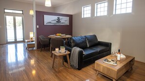 A modern living room with a black leather sofa, wooden coffee table, and a dining area with a table and chairs.