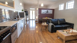 A modern kitchen with a built-in oven and microwave, a dining area with a black leather couch and a small wooden table, and a living room with a large painting on the wall.