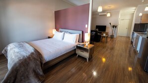 A modern hotel room with a large bed, bedside tables, a desk, and a kitchenette.