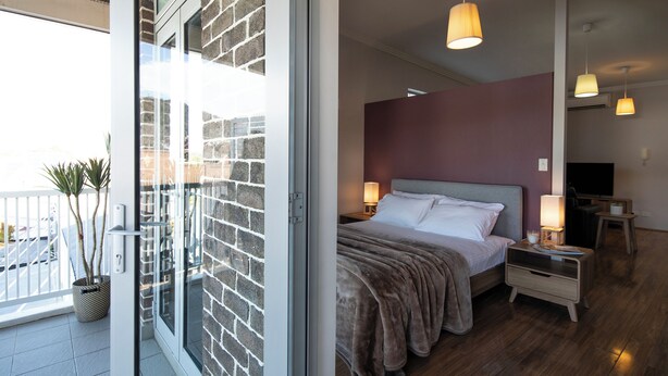 A hotel room with a bed, bedside tables, a TV, and a balcony with a potted plant.