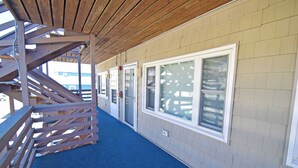 A covered outdoor corridor with a wooden staircase, beige walls, and large windows.