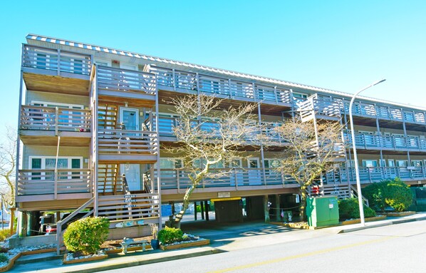 A multi-story hotel with balconies, a parking area, and a sign indicating a "Caution: Wet Floor" warning. - Old Wharf 15-AC,WIFI,W/D,Full kitchen (Ocean City)