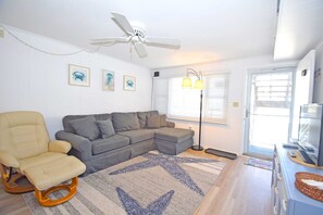 A living room with a sectional sofa, a rocking chair, a patterned rug, a ceiling fan, and a door leading outside. - Old Wharf 15-AC,WIFI,W/D,Full kitchen (Ocean City)