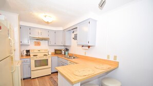 A compact kitchen with light blue cabinets, a wooden countertop, and two stools.