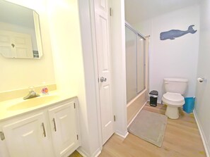 A bathroom with a white sink, mirror, and cabinets, a shower with a glass door, a toilet, and a blue trash bin. - Old Wharf 15-AC,WIFI,W/D,Full kitchen (Ocean City)