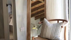 A wooden chair with a cushion in a room with a wooden staircase and a window with curtains.