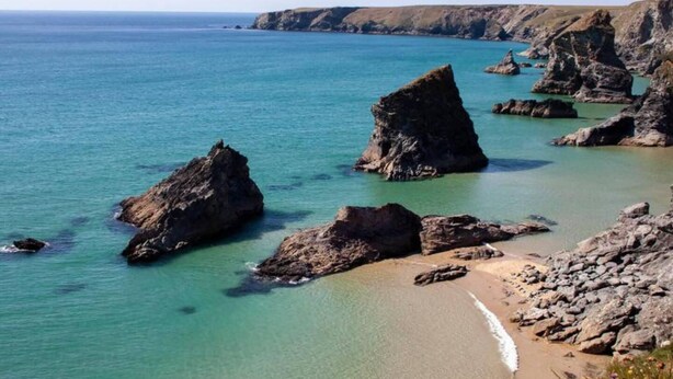 A coastal landscape with clear turquoise waters, rocky formations, and a sandy beach.