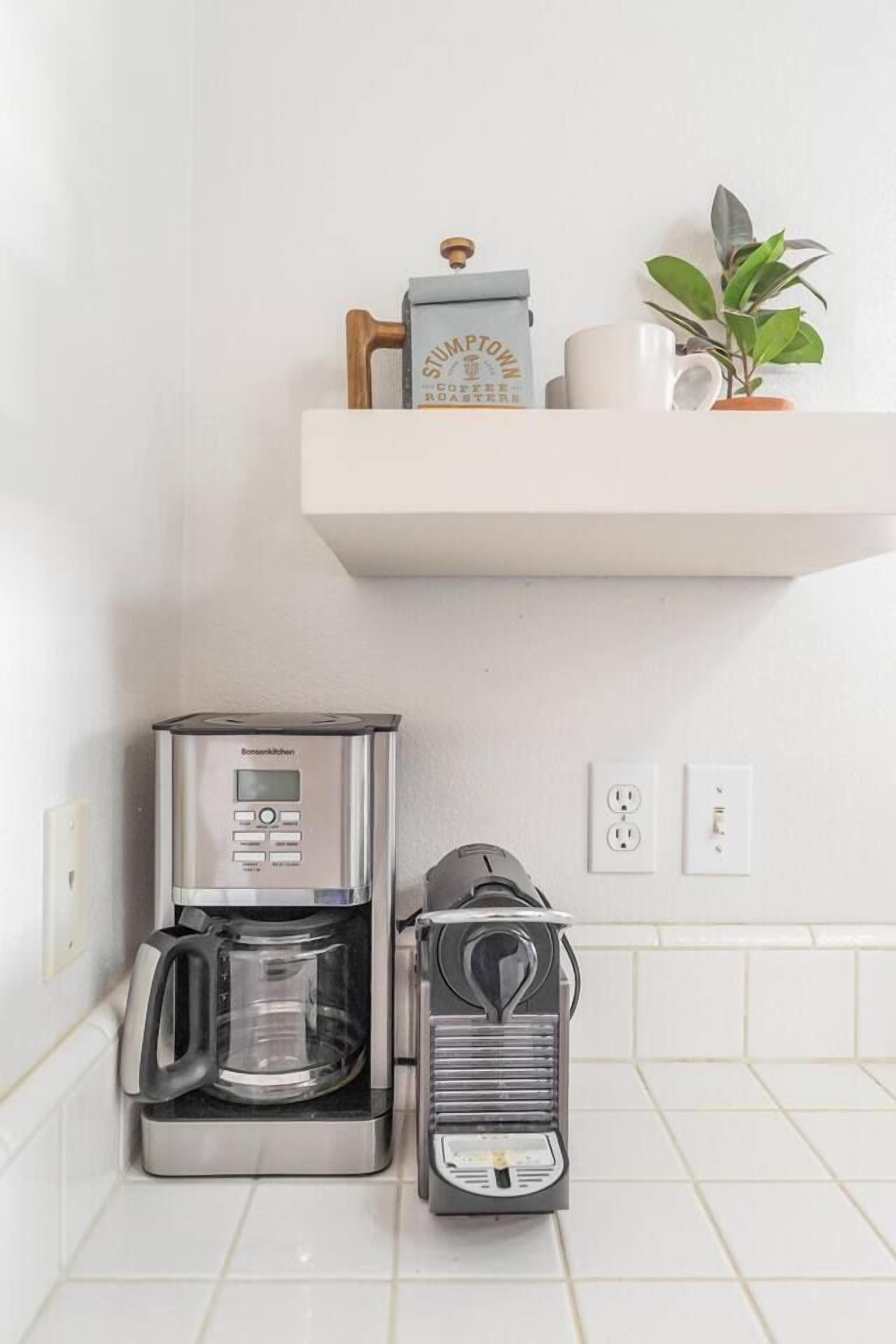 A kitchen with a coffee maker, a toaster, and a shelf with a coffee grinder and a mug.