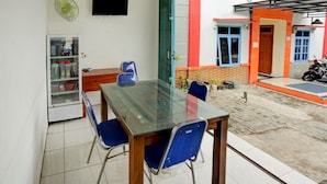 Un comedor con una mesa de vidrio, sillas azules, un refrigerador y un televisor en la pared.