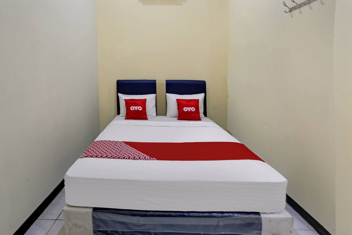Una cama individual con colchón blanco y ropa de cama rojo y blanco.
