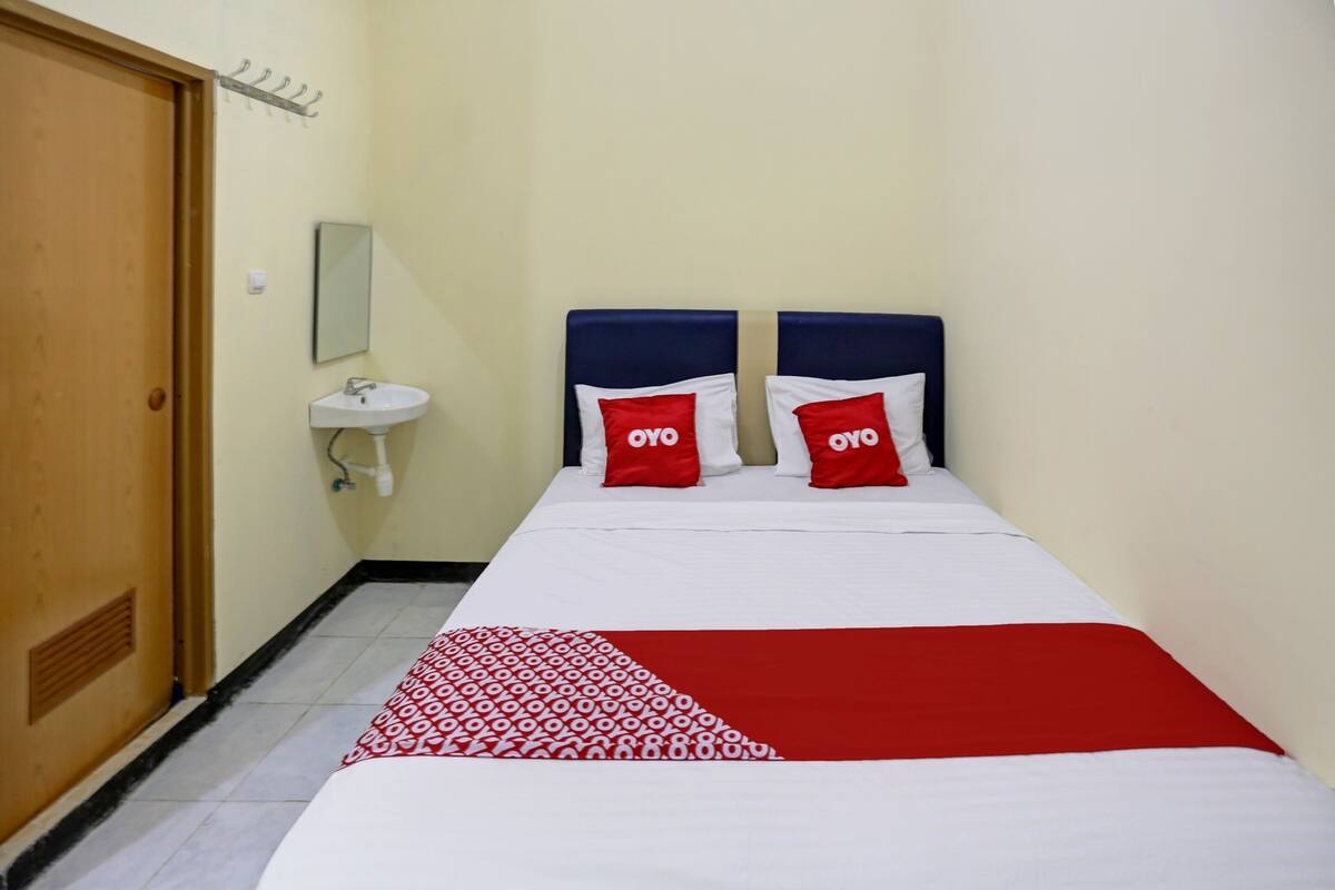 Habitación de hotel con una cama, dos almohadas con la marca 'OYO', una mesita de noche, un espejo y un lavabo.