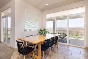 A dining area with a wooden table and black chairs, a potted plant, and a view through large glass doors.