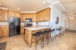 A kitchen with wooden cabinets, a black refrigerator, a microwave, and a bar area with stools.