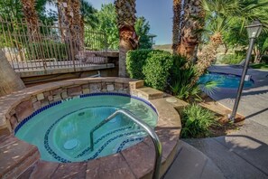 A hot tub with a tiled edge, surrounded by palm trees and a fence.