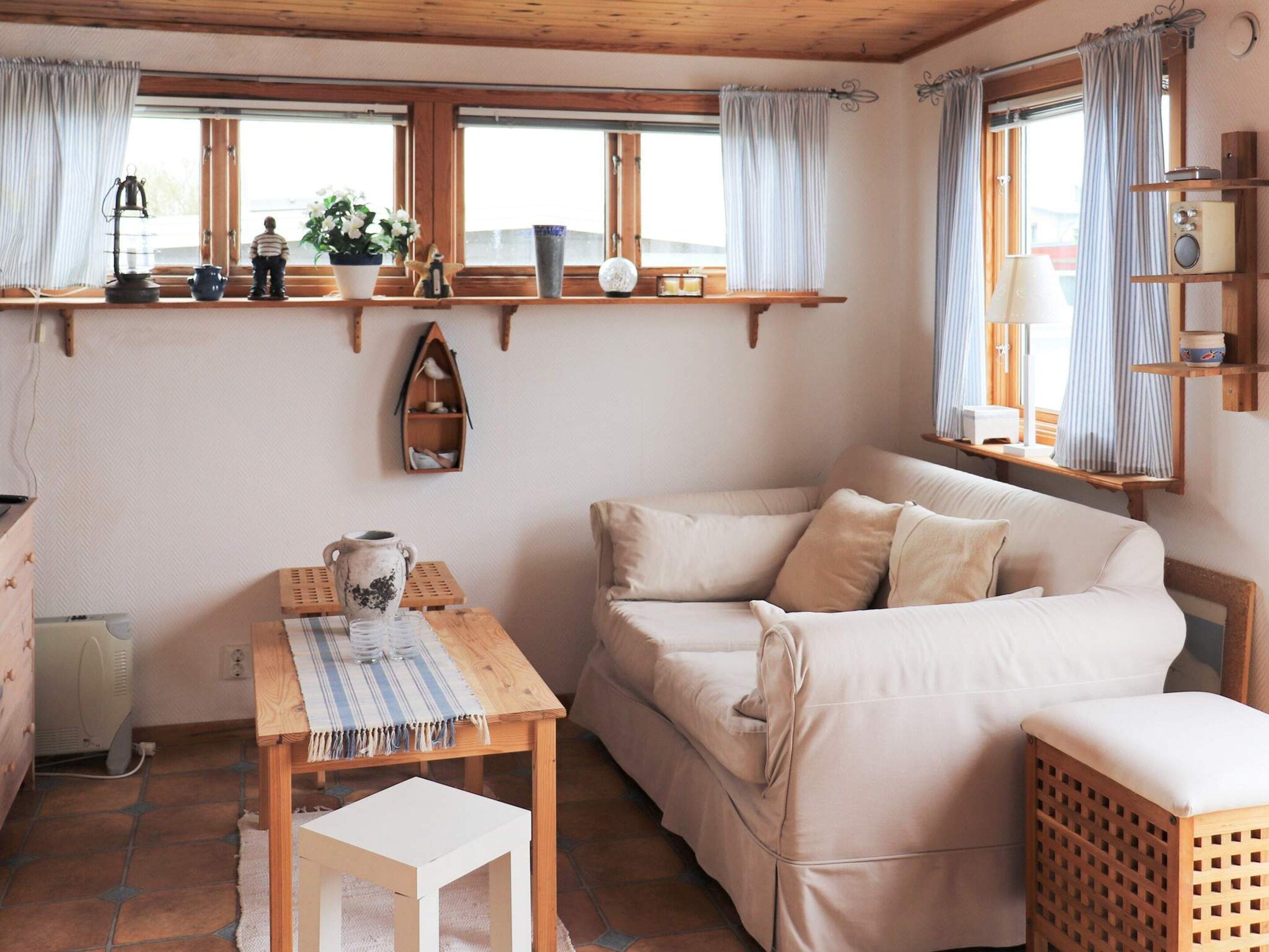 A cozy room with a sofa, a small table, a shelf with decorative items, and a window with curtains.