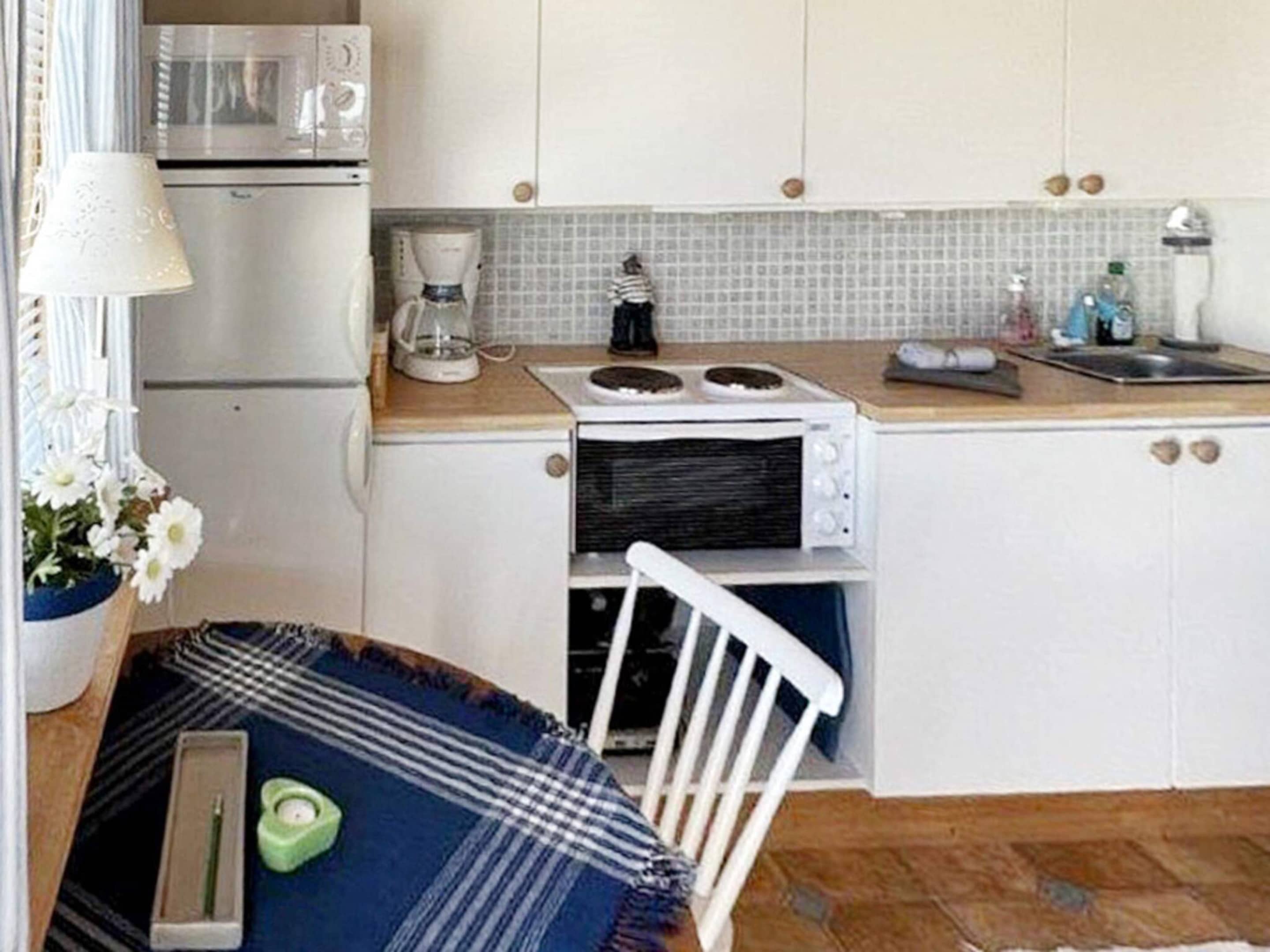 Cocina compacta con muebles blancos, microondas, cafetera y un pequeño comedor con una silla y una mesa.