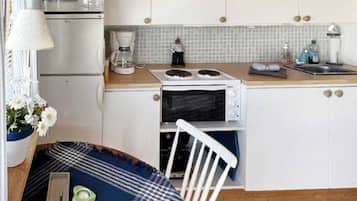 Cocina compacta con muebles blancos, microondas, cafetera y un pequeño comedor con una silla y una mesa.