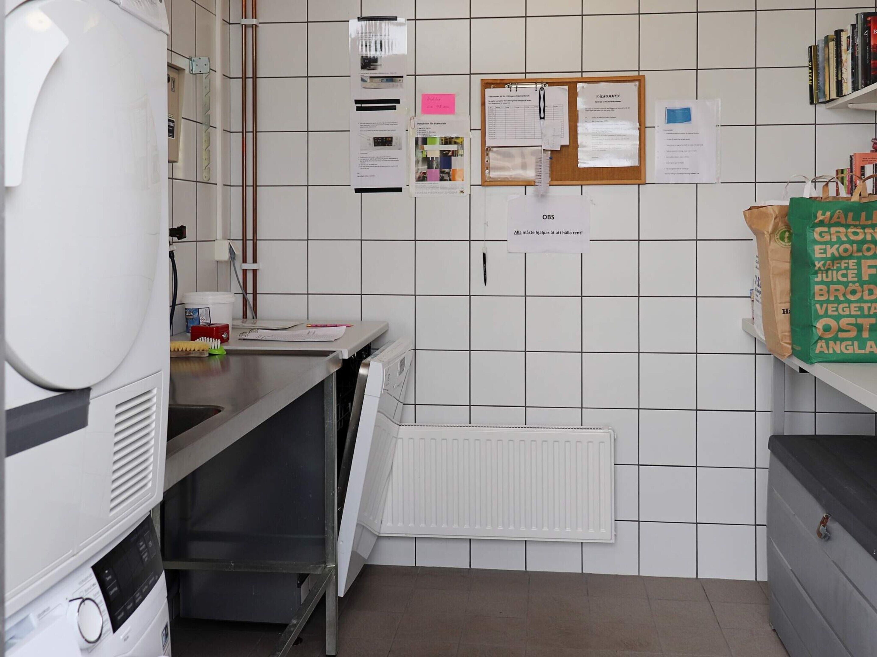 Una cocina con un refrigerador blanco, un lavamanos, un lavavajillas y un tablón de anuncios con varios avisos.