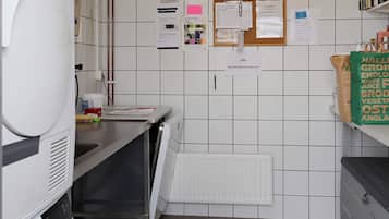 Una cocina con un refrigerador blanco, un lavamanos, un lavavajillas y un tablón de anuncios con varios avisos.