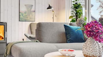 Una sala de estar moderna con un sofá gris, una mesa redonda de madera con cuencos, un jarrón decorativo y una chimenea.