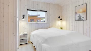 Et soveværelse med seng, vindue, et natbord, en lampe og et billede i ramme på væggen.