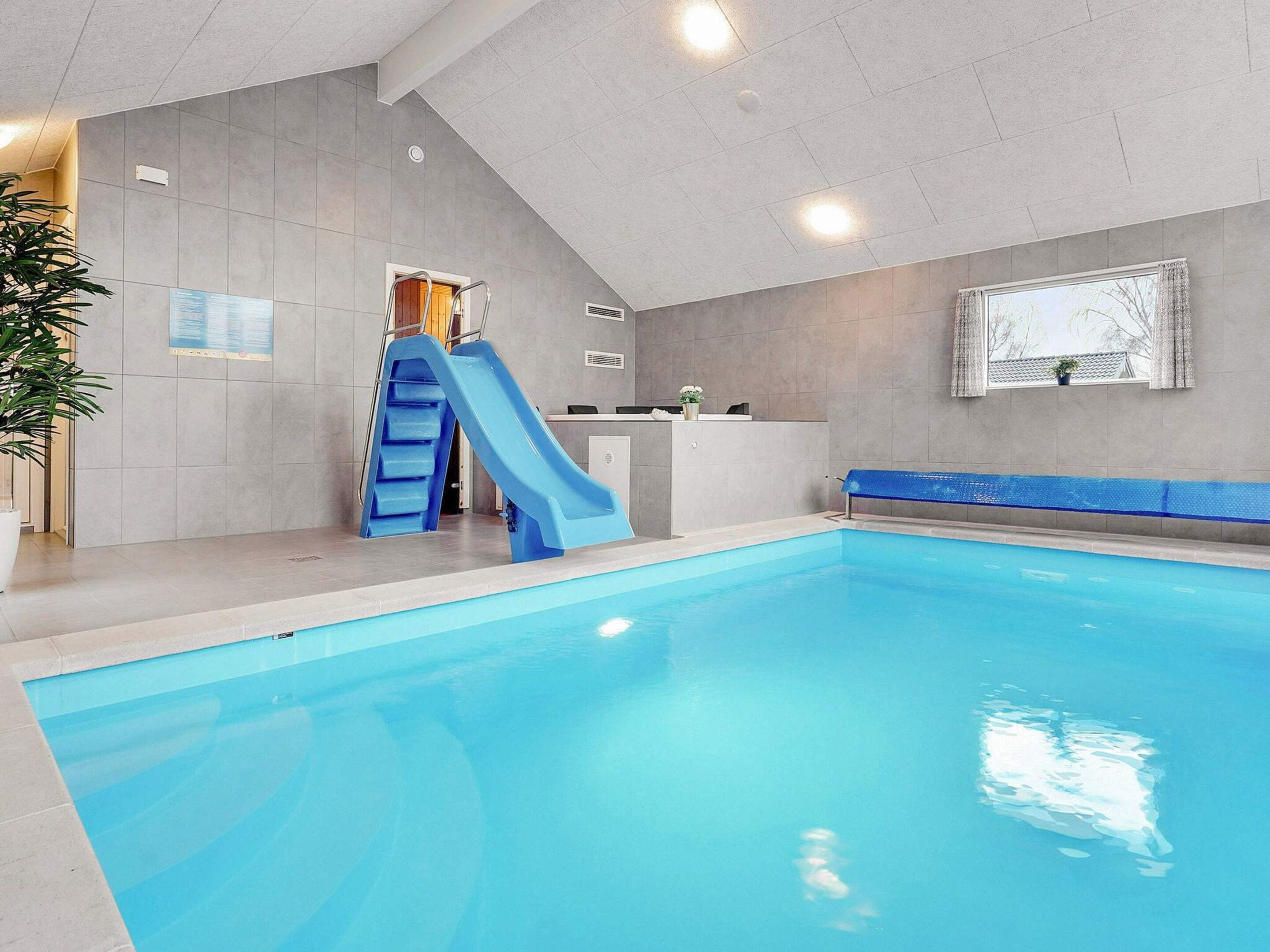 An indoor swimming pool with a blue slide, a reception desk, and a window with a view.