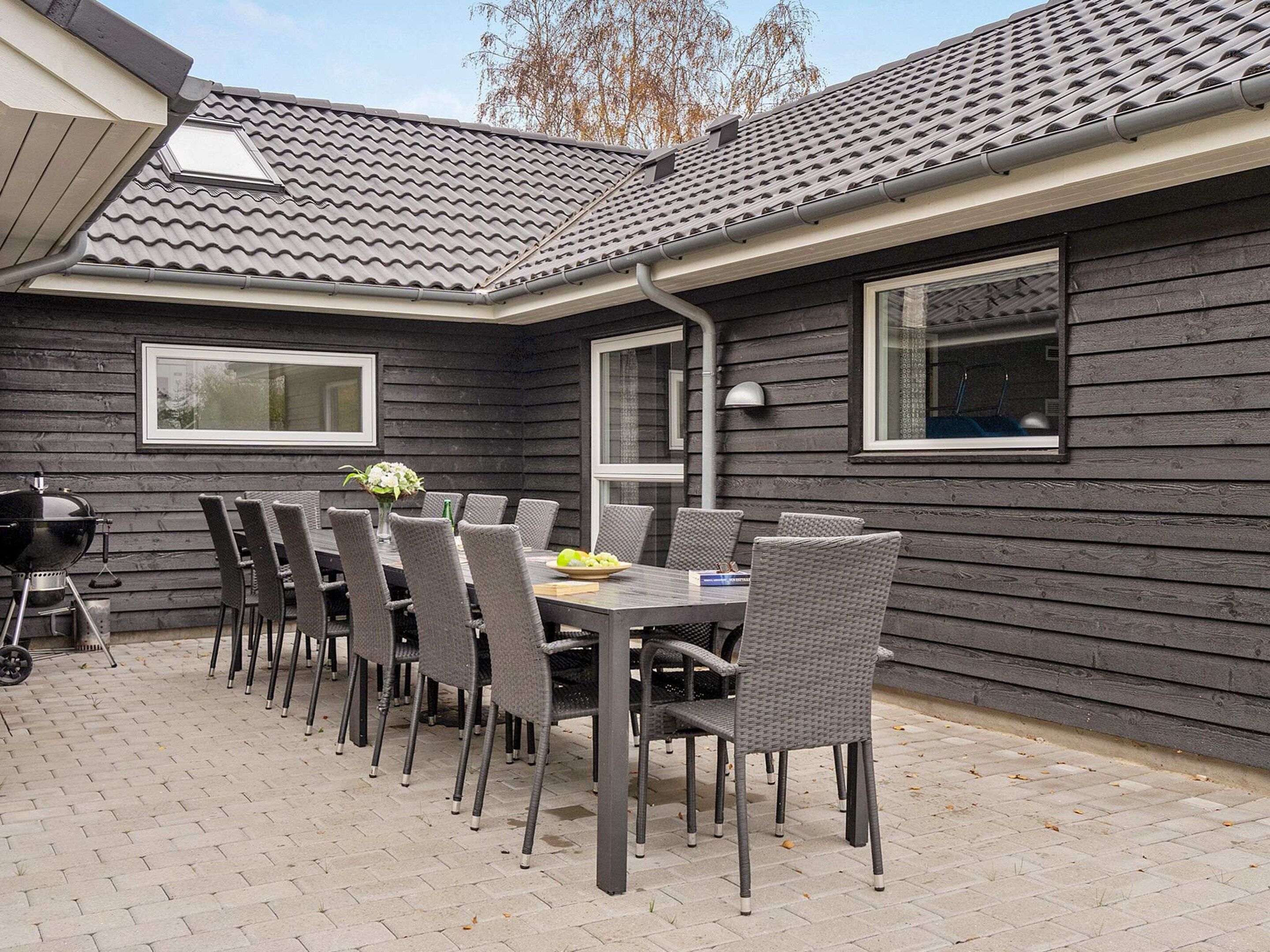 An outdoor patio with a table and chairs, a grill, and a window.