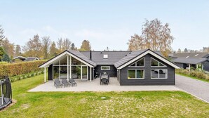 Een modern huis met twee verdiepingen, een overdekte patio, grote ramen en een verzorgd gazon.