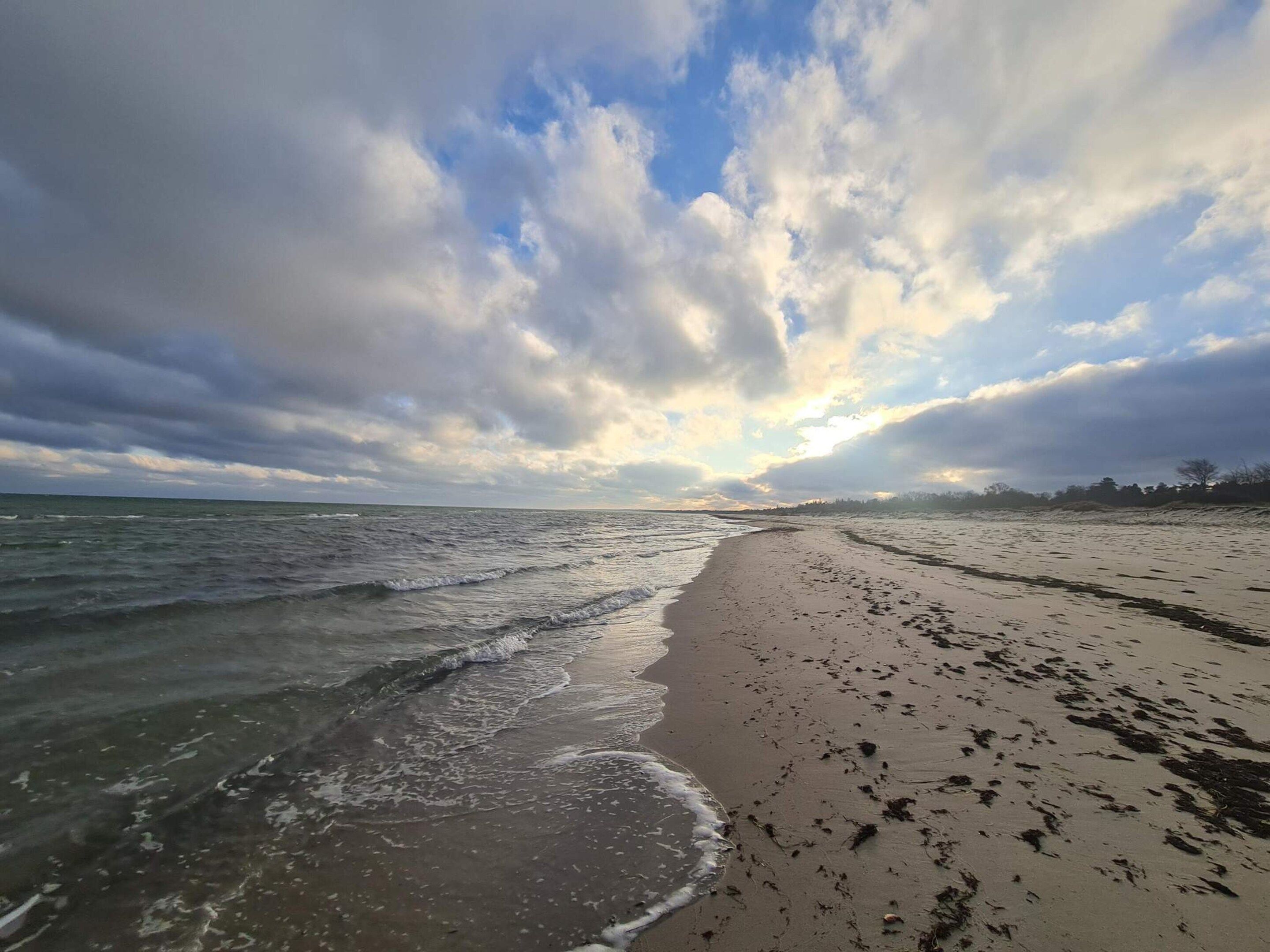 A beach with waves, a sandy shore, and a partly cloudy sky.