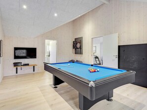 Una mesa de billar con bolas, un televisor y un dardo en una habitación con paredes de madera y una lámpara en el techo.