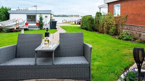 A patio with wicker furniture, a bottle of wine, and a glass. - 2 Person Holiday Home in Grasten (Grasten)