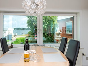 Une table à manger avec une bouteille de vin Black Tower, un verre et des sets de table, donnant sur un jardin avec vue sur un lac et un bâtiment en briques.