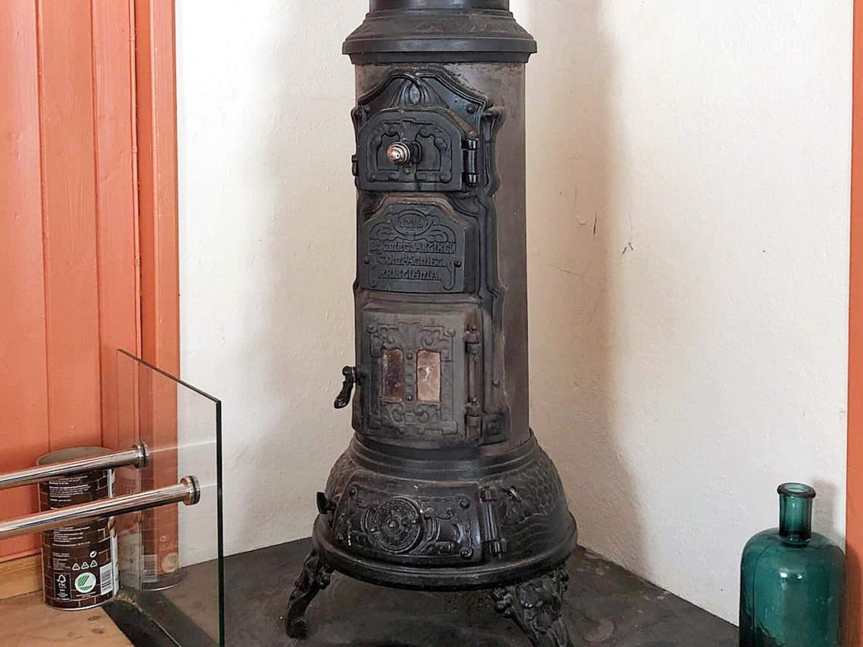A black stove with intricate designs and a control panel, placed against a white wall with a wooden panel on the left.