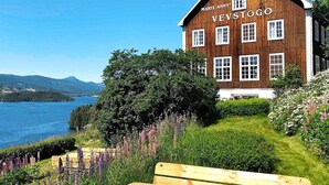A wooden building with the name "Marit Annby Vevstogo" on its facade, situated by a lake with a bench in the foreground. - 5 Person Holiday Home in Lomen-by Traum (Vestre Slidre)