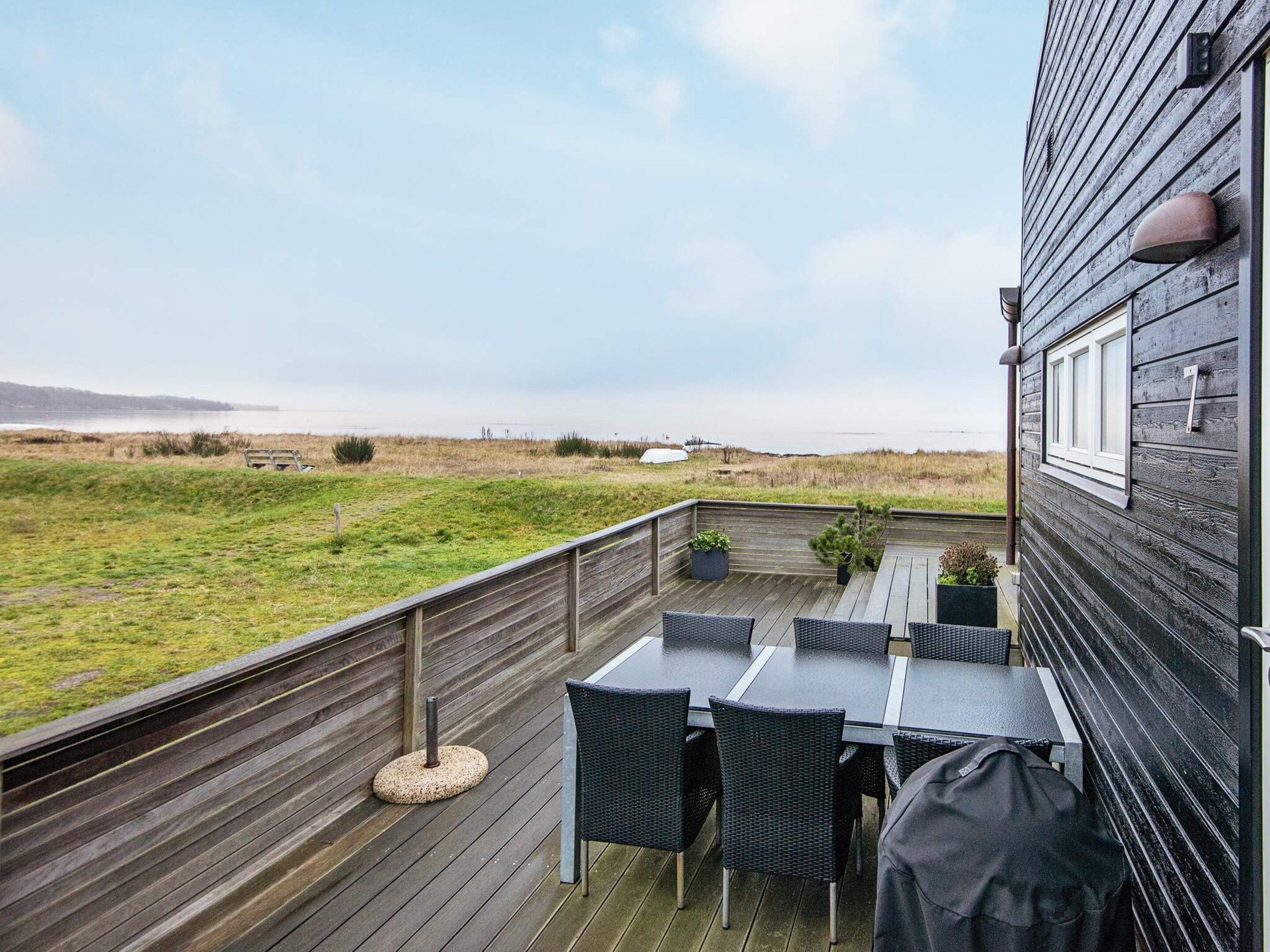 An outdoor deck with a table and chairs, overlooking a grassy area and the sea.
