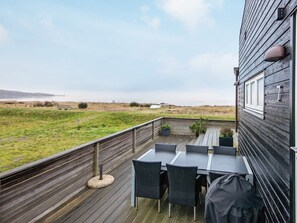 Terraza exterior con mesa y sillas, con vistas a un césped y el mar.