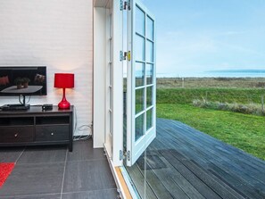 A room with a television, a red lamp, and a large window overlooking a grassy area. - 4 Star Holiday Home in Juelsminde (Juelsminde)