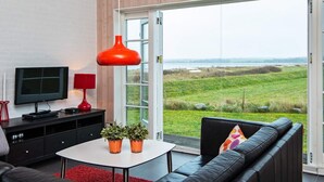Un salón moderno con televisor, lámpara roja y vista a un campo verde a través de un ventanal.