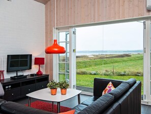 A modern living room with a television, red lamp, and a view of a grassy field through a glass door. - 4 Star Holiday Home in Juelsminde (Juelsminde)