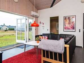 Una sala de estar moderna con un sofá de cuero negro, una lámpara colgante roja y un ventanal con vistas al exterior.